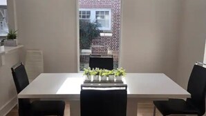 Un comedor con una mesa blanca, sillas negras y plantas en macetas.
