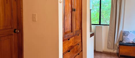 A hallway with wooden doors, a tiled floor, a window with a view of greenery, and a bench with a cushion.