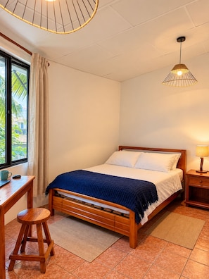 Ein Schlafzimmer mit einem hölzernen Bett, einem Schreibtisch, einem Stuhl, einer Pendelleuchte und einem Fenster mit Vorhängen.