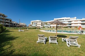 A poolside area with lounge chairs, a pool, and a modern building with balconies. - Los Colibríes by H - Isla Canela Golf GLHC7023P98 (Ayamonte)