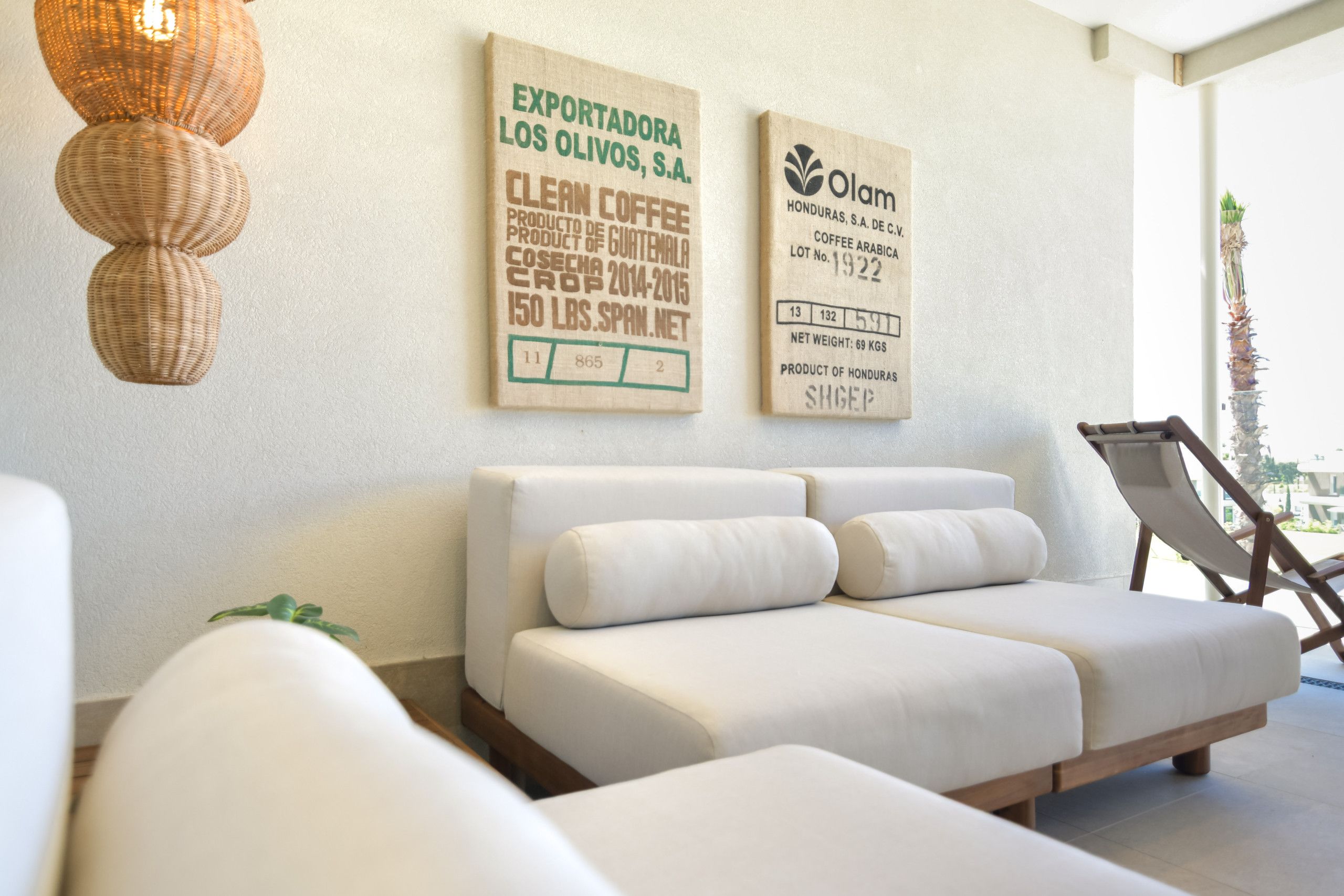 A modern lounge area with a white sofa and a lounge chair, a woven light fixture, and two wall-mounted signs indicating coffee products from Honduras.