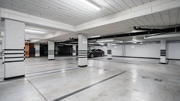 Un aparcamiento de varios niveles con pilares de hormigón, un coche estacionado en una de las plazas y luces en el techo.