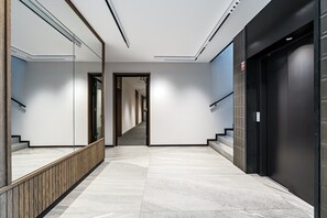 A modern hallway with a marble floor, a wooden railing, and a black elevator door. - Oh Baby - Premium with Relaxing Bathtub (Gdańsk)