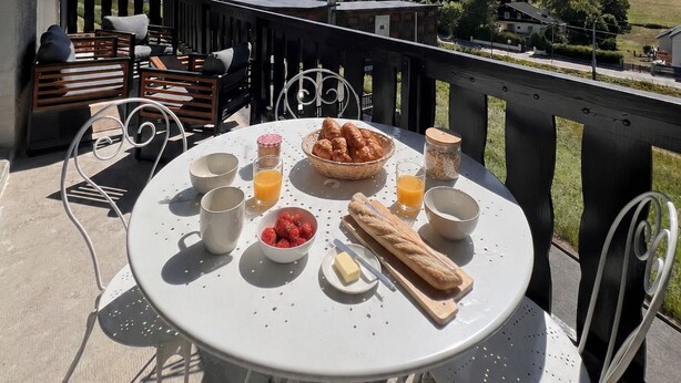 Ein Tisch draußen gedeckt mit Frühstücksgebäck, mit Blick auf eine Berglandschaft.