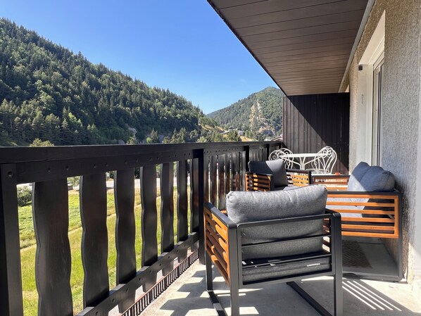 Un balcon doté de balustrades en bois, d’un canapé et d’un fauteuil, offrant une vue sur un paysage montagneux.