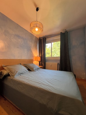 A bedroom with a single bed, a bedside lamp, a window with curtains, and a radiator. - Le Narcisse—Mountain View, Sleeps 6, Quiet, Ski Shuttle (Villard-de-Lans)