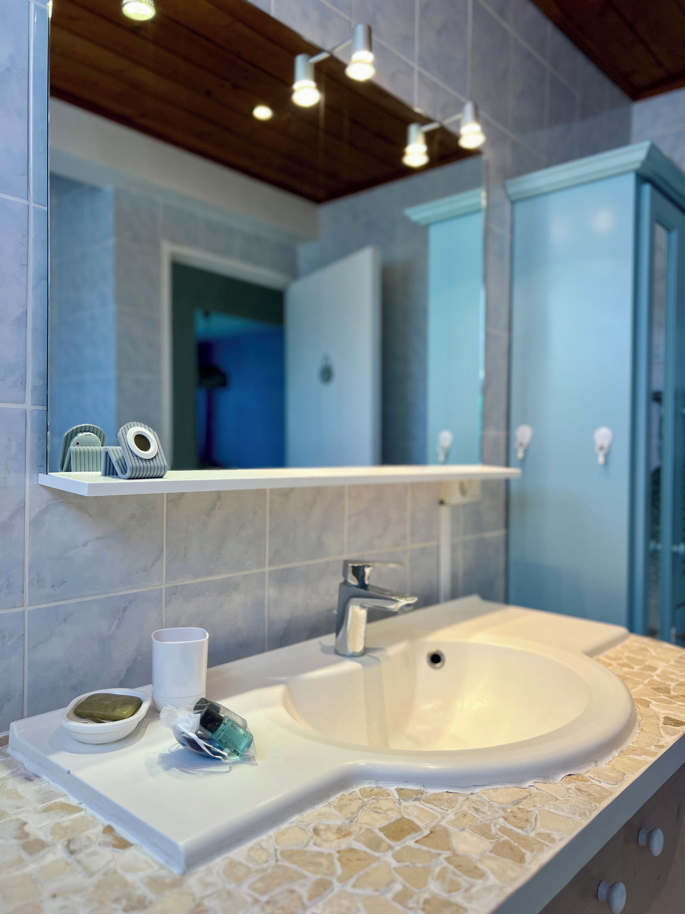 Un baño con un lavabo blanco, un espejo y un estante con artículos de aseo.