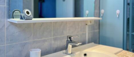 Un baño con un lavabo blanco, un espejo y un estante con artículos de aseo.