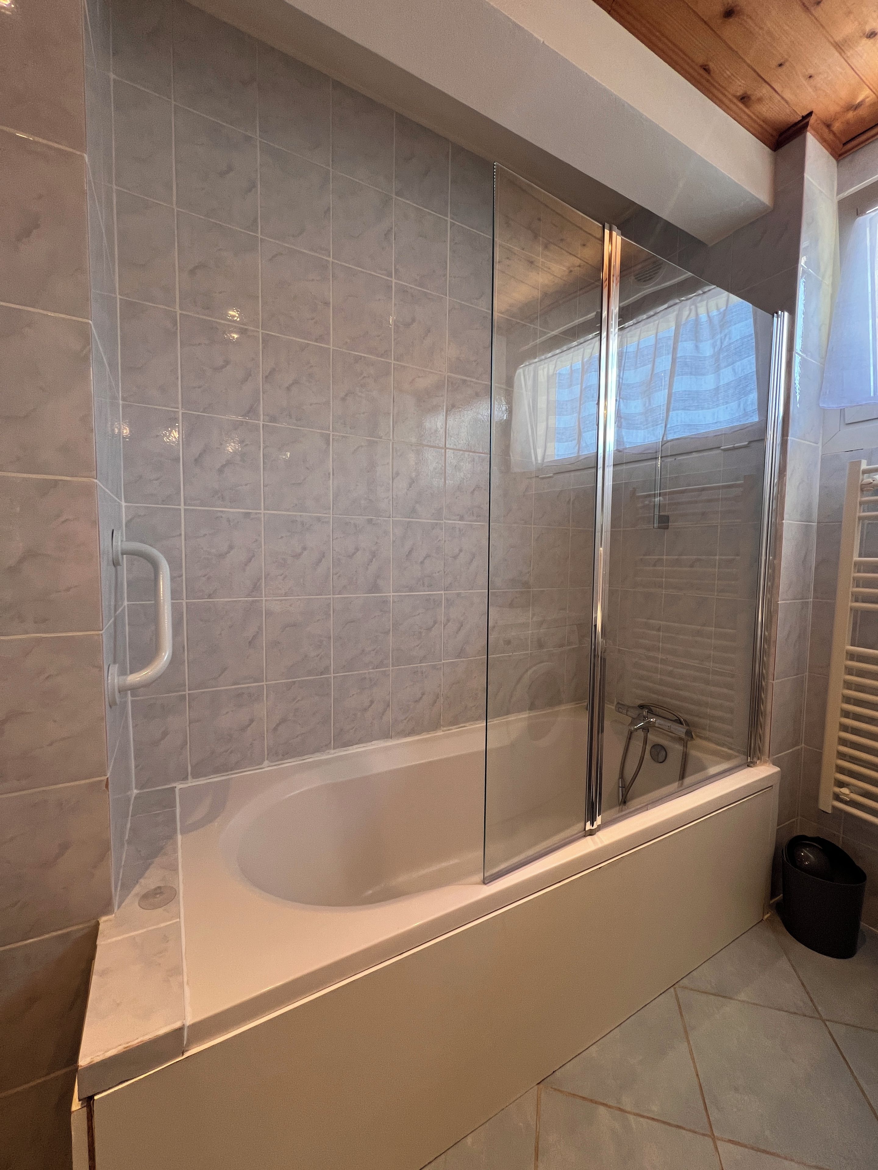 A modern bathroom with a glass-enclosed bathtub, tiled walls, and a wooden ceiling.