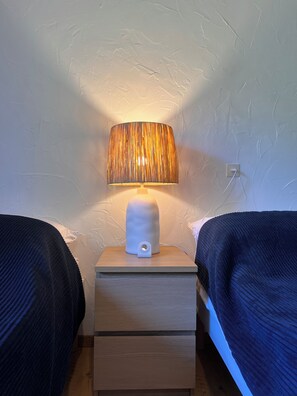 Une chambre avec deux lits, une table de chevet avec une lampe et une prise électrique au mur.
