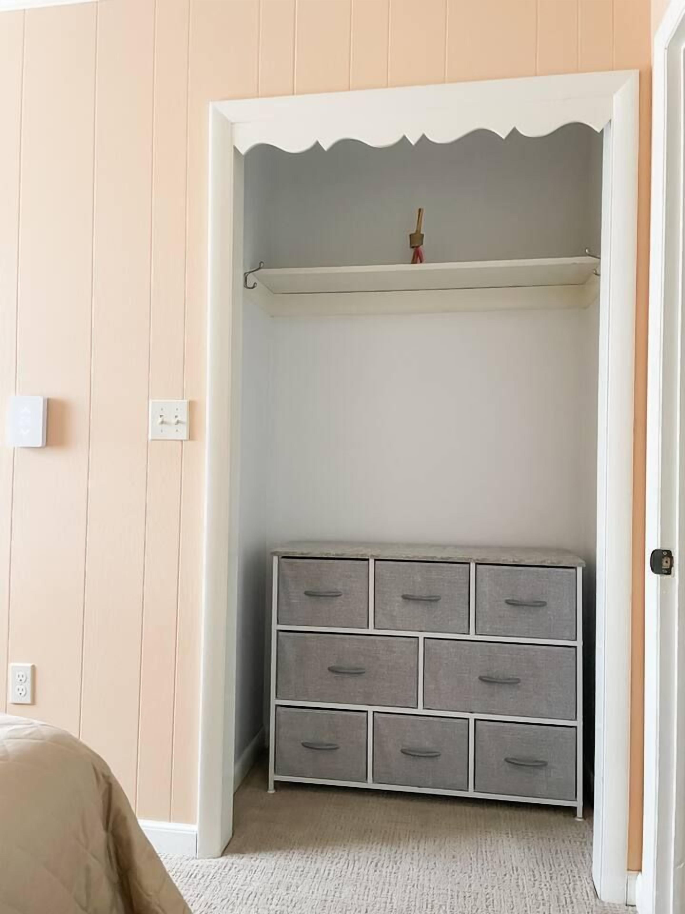 Ein Zimmer mit einem Kleiderschrank, der mehrere Schubladen und eine Kleiderstange bietet.