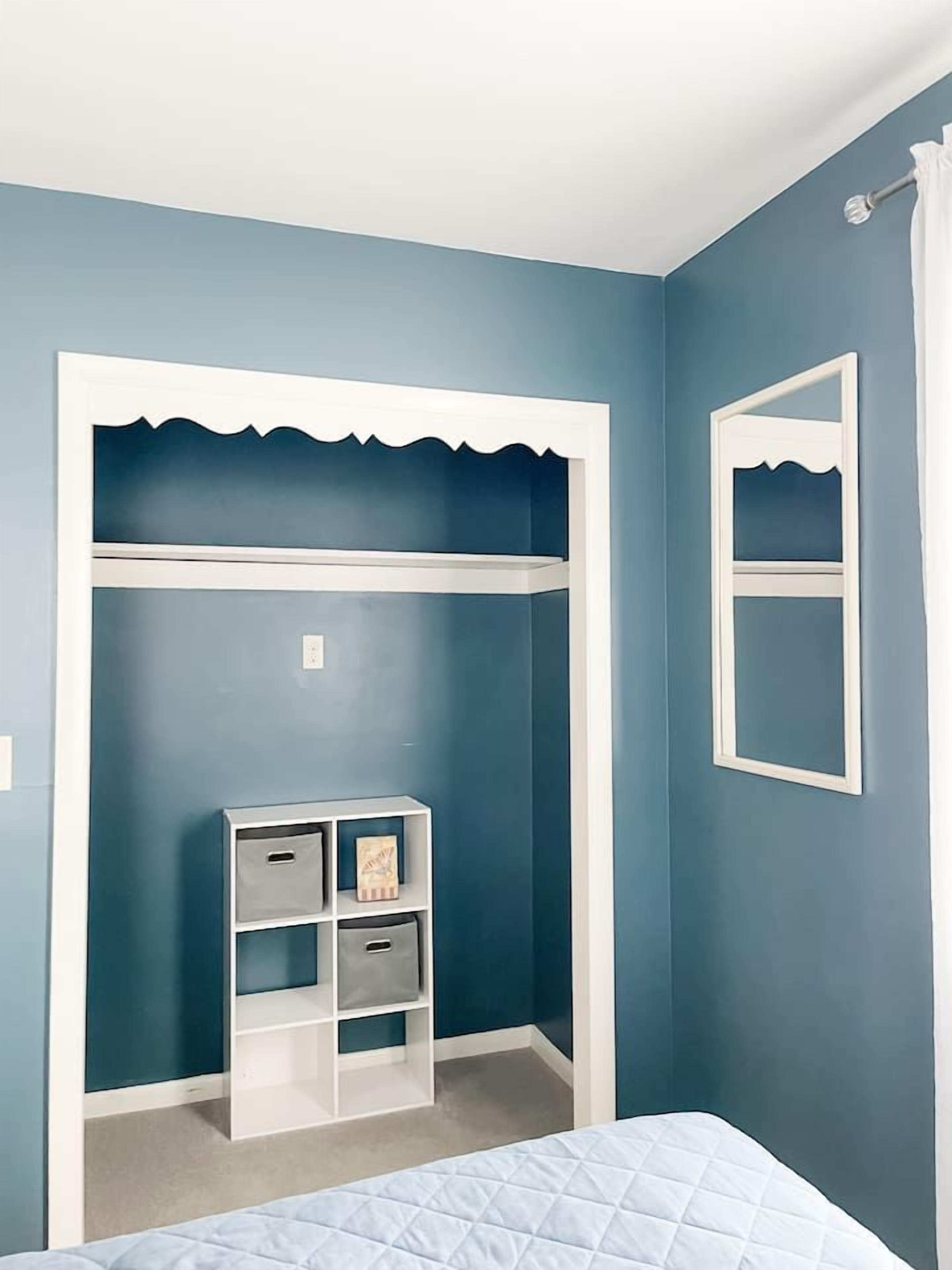 Une chambre à coucher avec un lit, une armoire à ossature blanche et un miroir au mur.