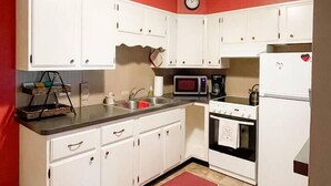 Una cocina compacta con armarios blancos, un microondas, una estufa y un refrigerador.