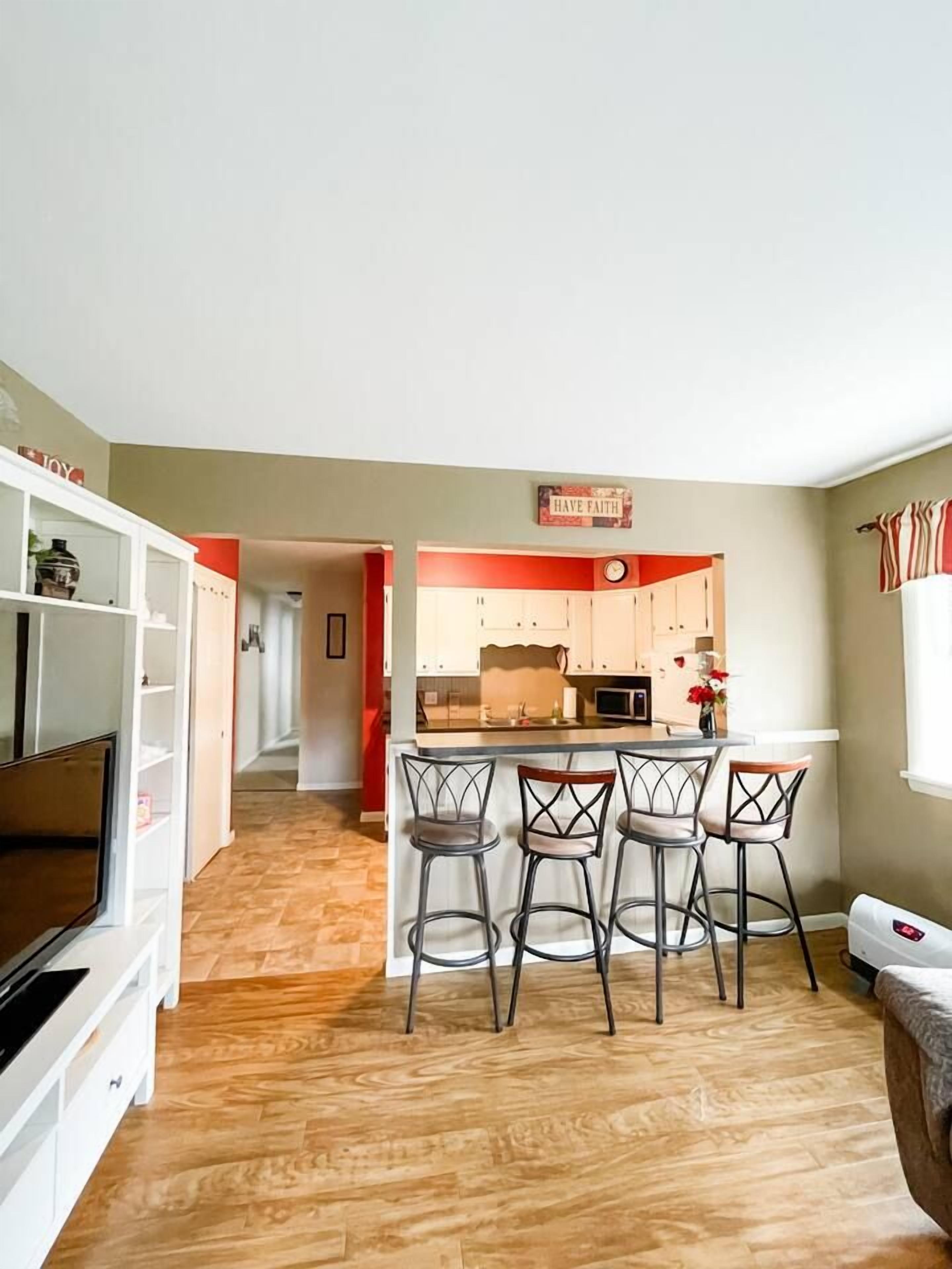 A modern kitchen with a bar area, wooden flooring, and a TV in the living room.