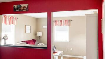 A room with a bed, a desk, a chair, a window with curtains, and a door.