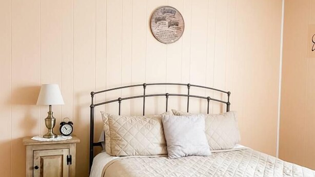 Un dormitorio con cama, mesita de noche, lámpara, reloj y ventilador de techo.