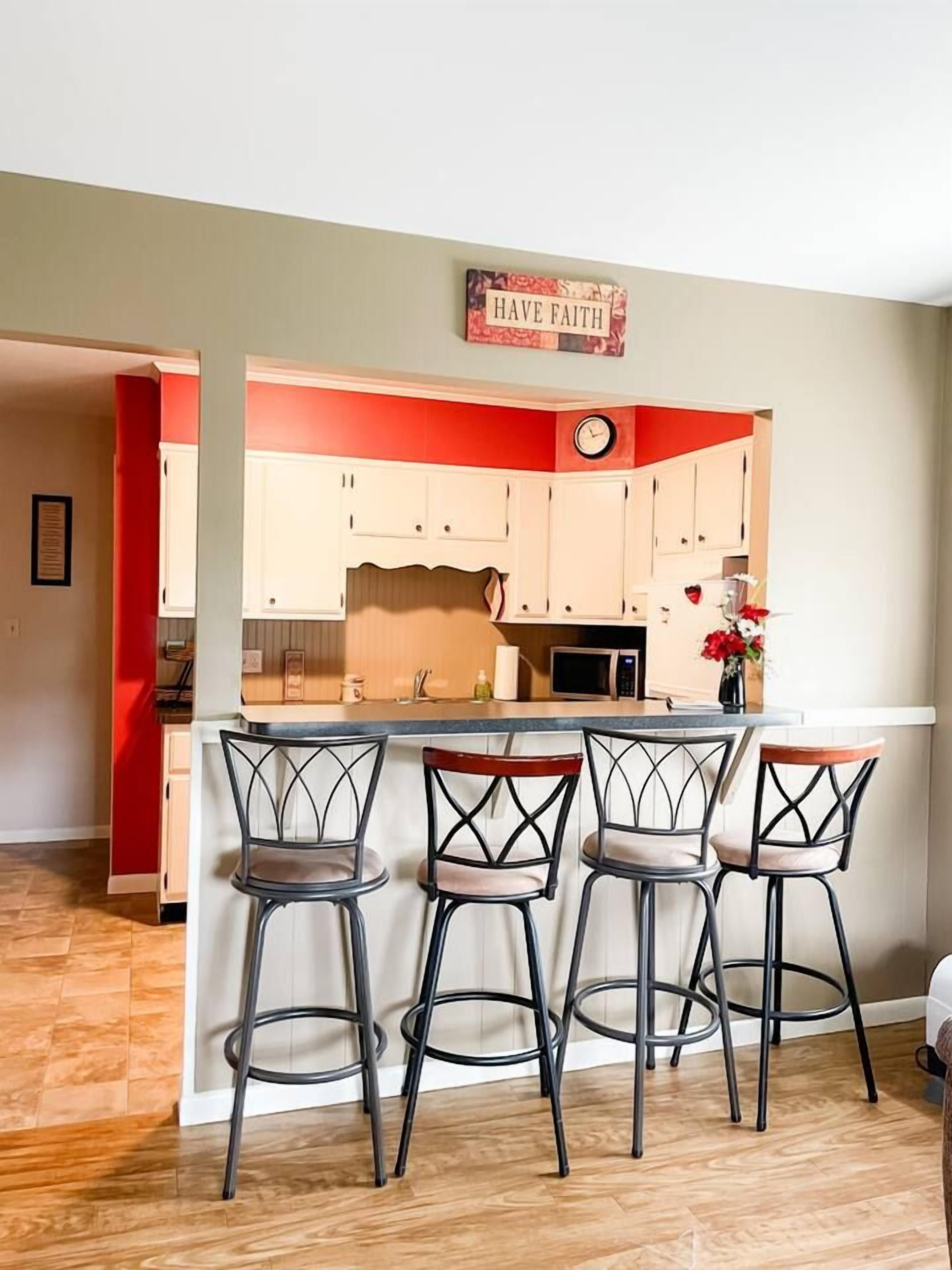 A kitchen with a red accent wall, a clock, and three bar stools.