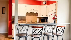 Una cocina con una pared de acento roja, un reloj y tres taburetes de bar.