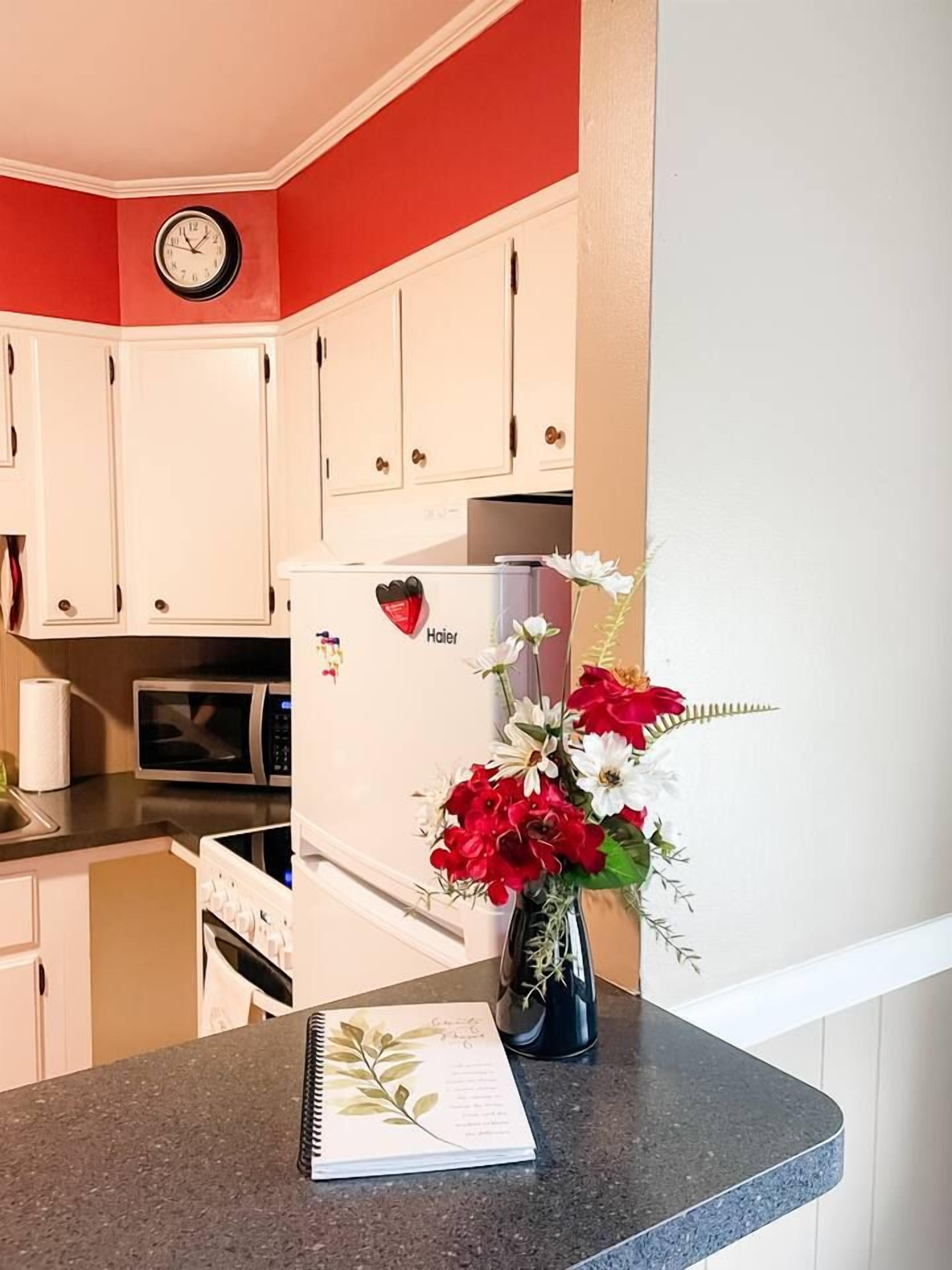 A kitchen with white cabinets, a white refrigerator, a clock on the wall, and a vase with flowers on the counter.