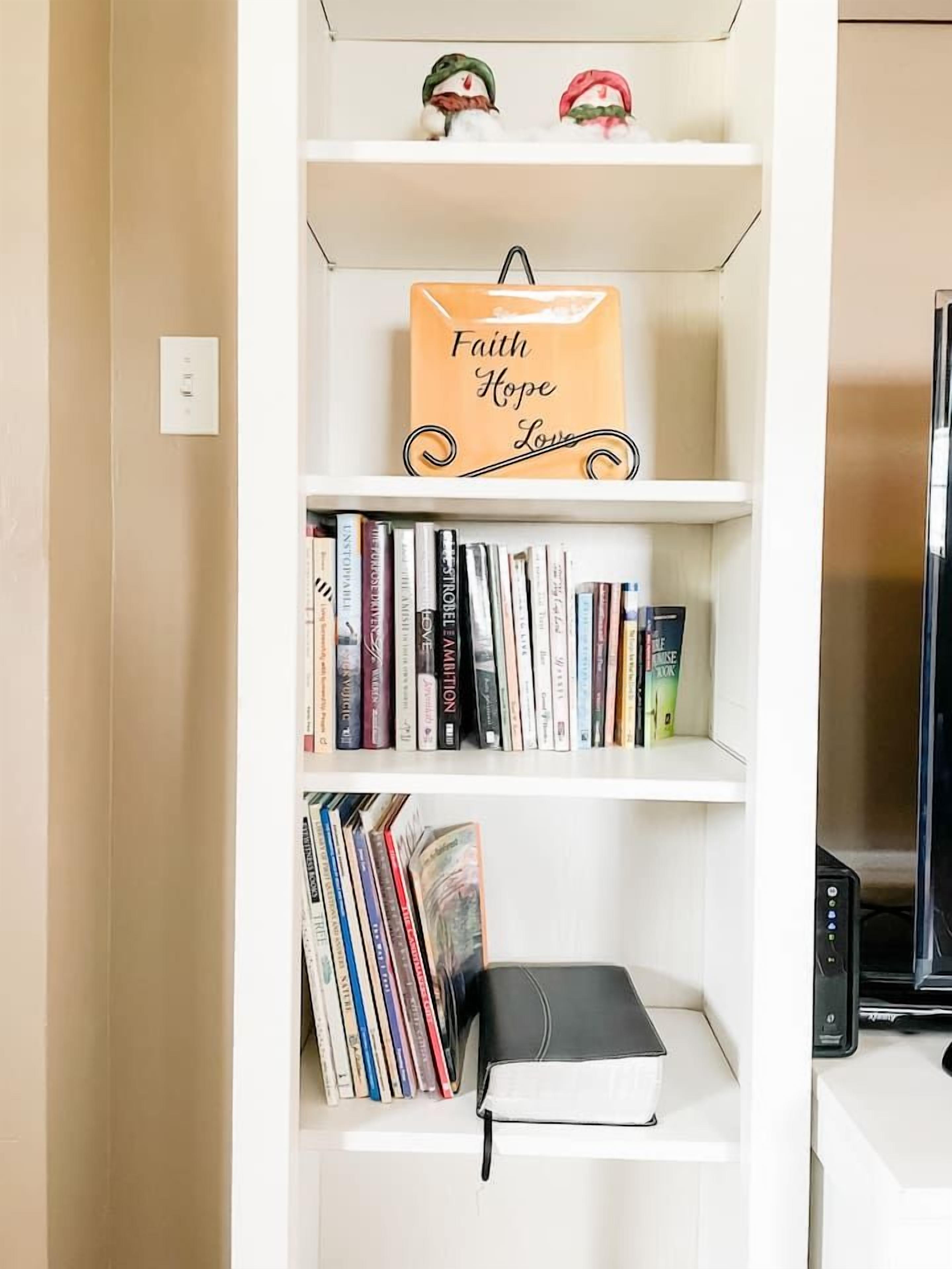 Una estantería con libros y un letrero decorativo que dice 'Faith Hope Love'.