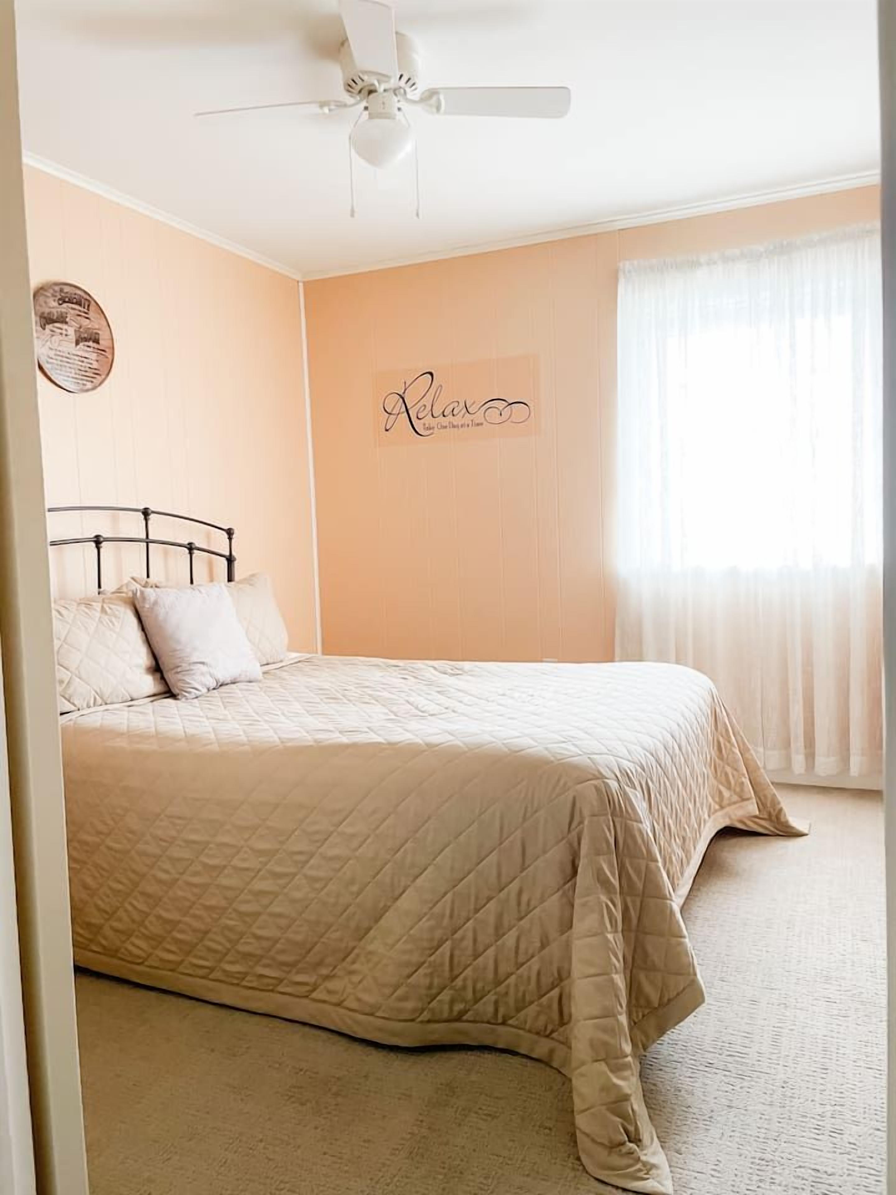 A bedroom with a bed, a ceiling fan, a wall with a sign, and a window with curtains.
