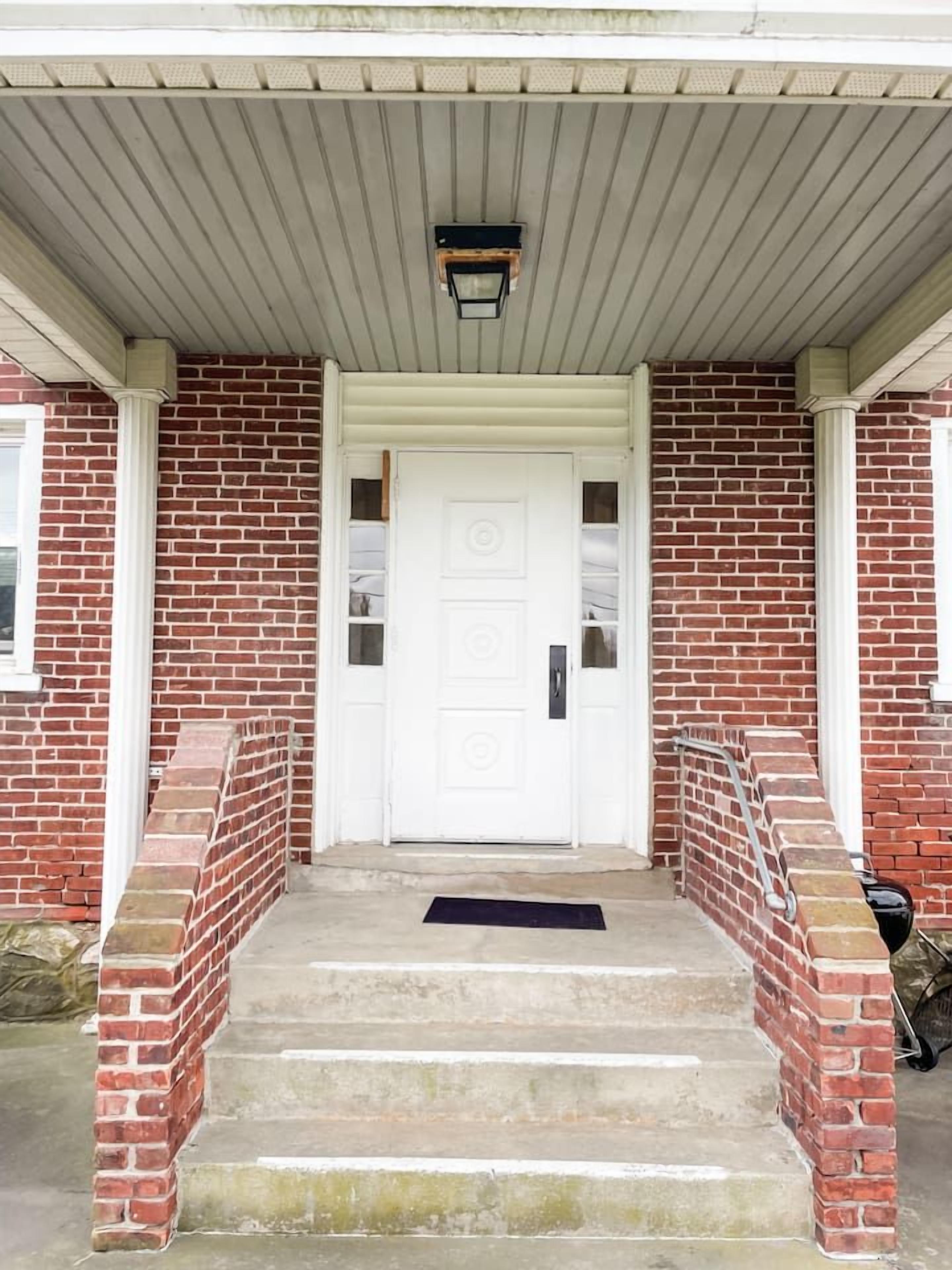 A brick house with a white front door, a set of concrete steps, and a small porch area.