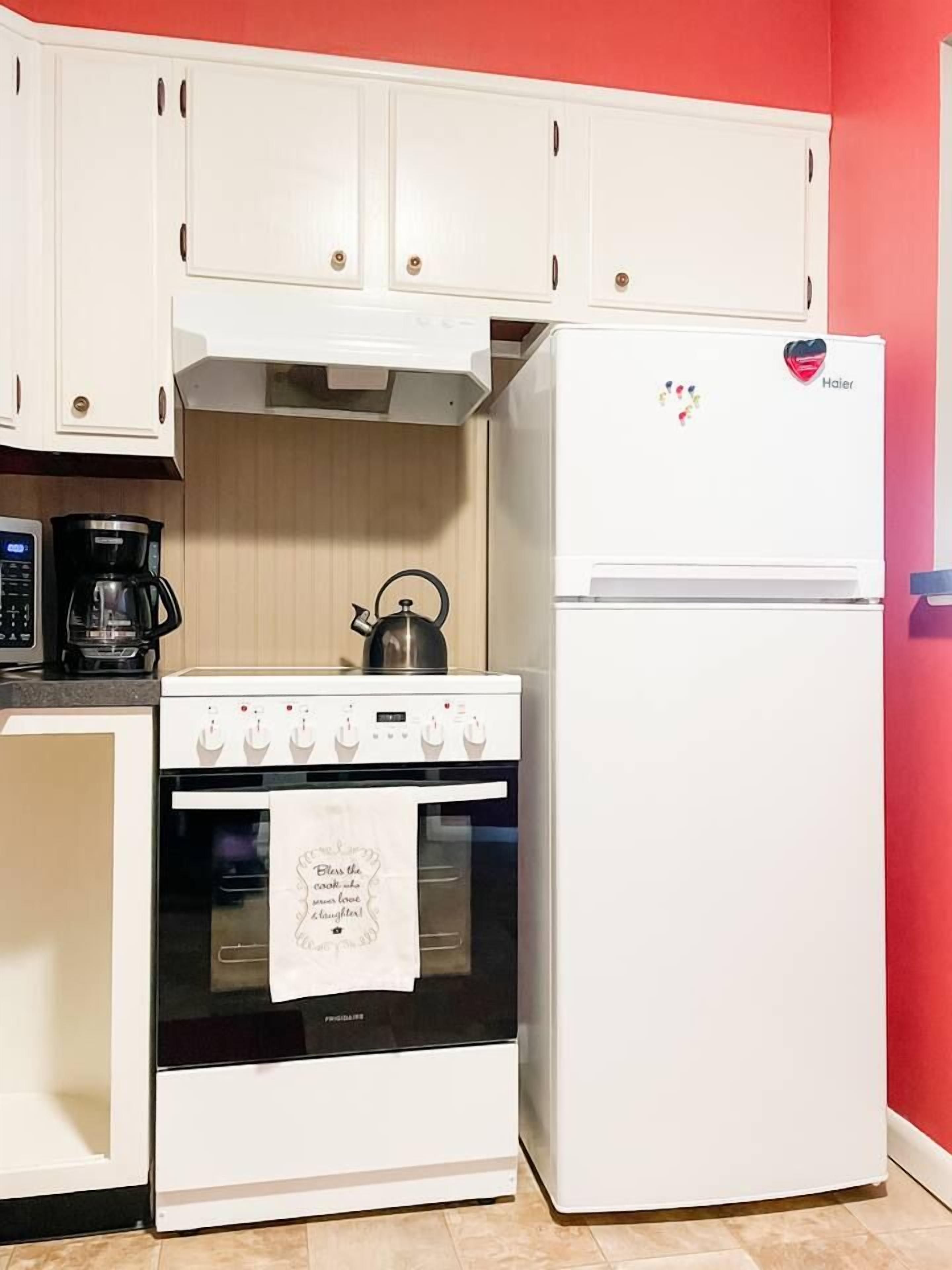 Una cocina con estufa, horno y refrigerador blancos, una tetera y una cafetera.