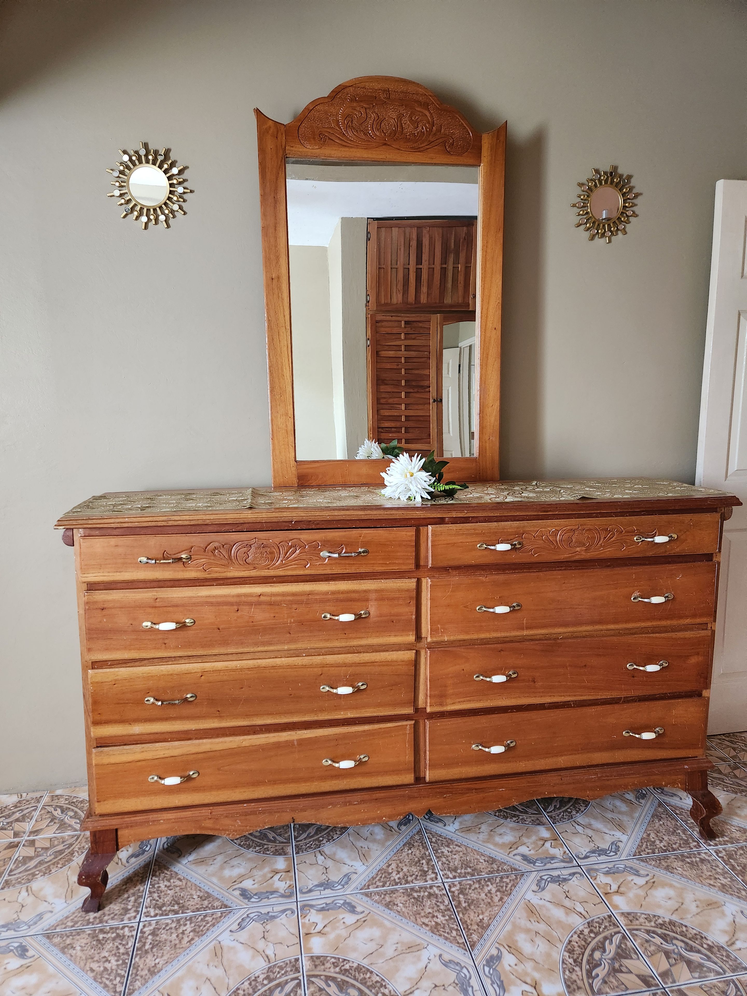 A wooden dresser with a mirror and decorative sunburst wall sconces.