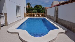 Ein rechteckiger Swimmingpool mit weißer Umrandung und einem Holenzaun im Hintergrund.