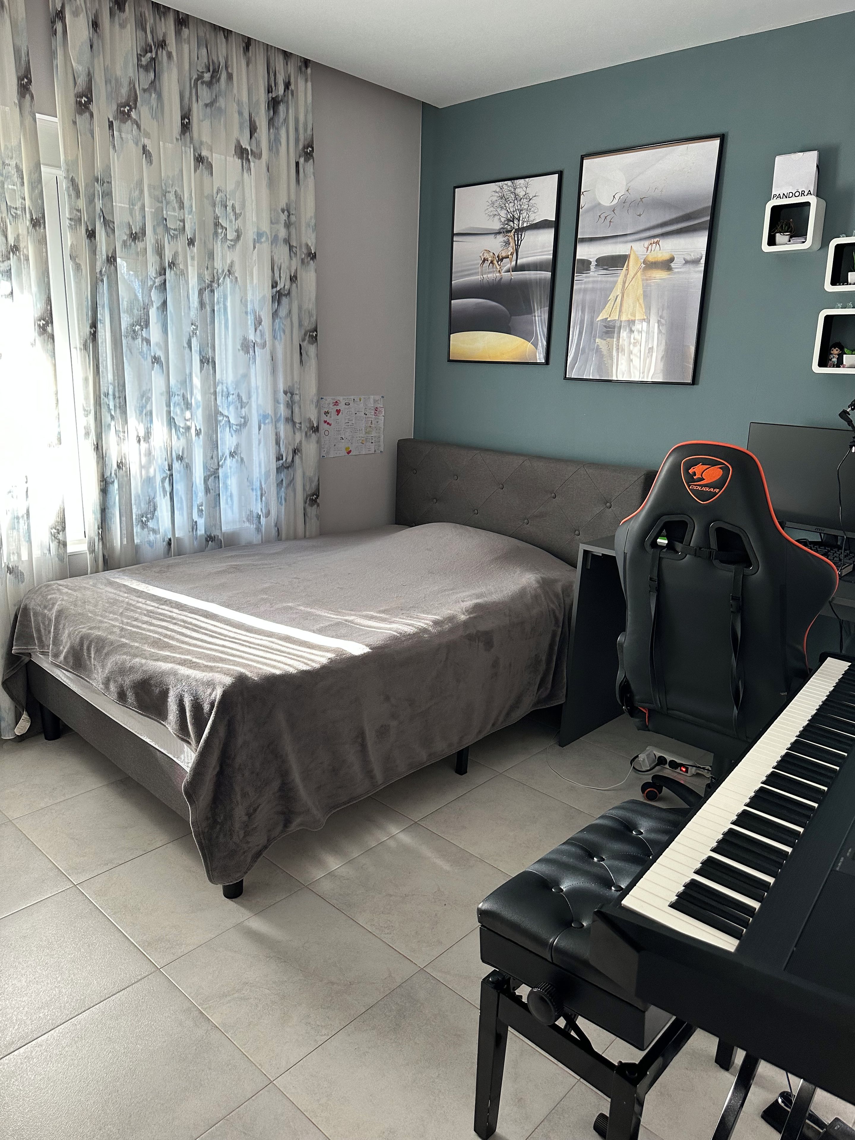 Une chambre à coucher avec un lit, un bureau avec un clavier, un fauteuil de jeu et des œuvres d’art accrochées au mur.