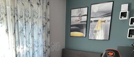 Une chambre à coucher avec un lit, un bureau avec un clavier, un fauteuil de jeu et des œuvres d’art accrochées au mur.