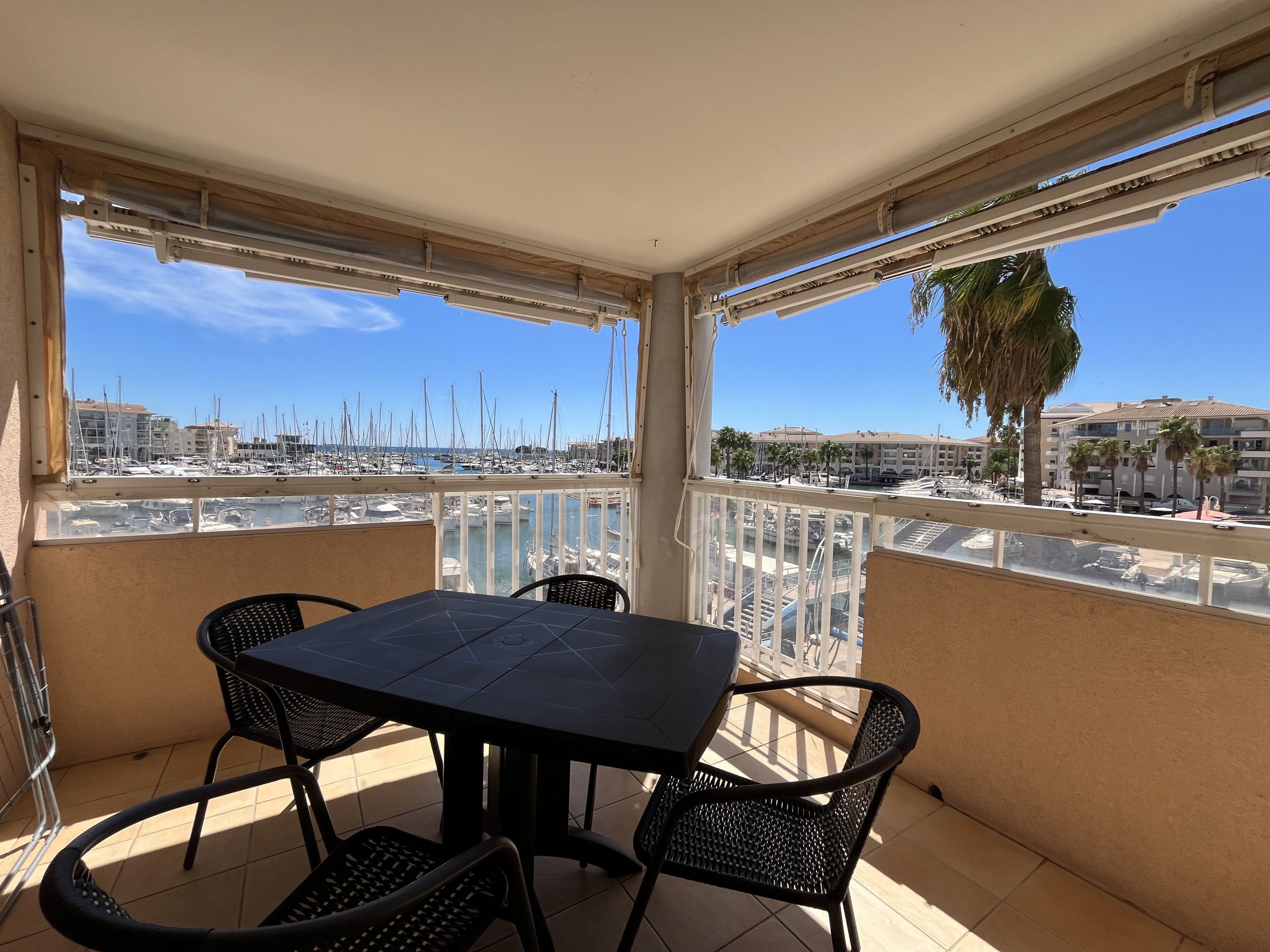Un balcón con mesa y sillas, con vistas a una marina llena de barcos y edificios.