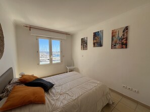 A bedroom with a bed, a chair, a window with a view of a marina, and three paintings on the wall. - Port Fréjus: magnificent 1-bedroom apartment with a harbor view, sleeping 4; lively area, air-conditioned, with Wi-Fi and parking. (Fréjus)