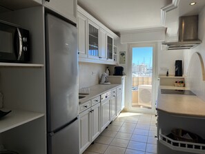 A modern kitchen with white cabinetry, a stainless steel refrigerator, and a view of the city through an open door. - Port Fréjus: magnificent 1-bedroom apartment with a harbor view, sleeping 4; lively area, air-conditioned, with Wi-Fi and parking. (Fréjus)