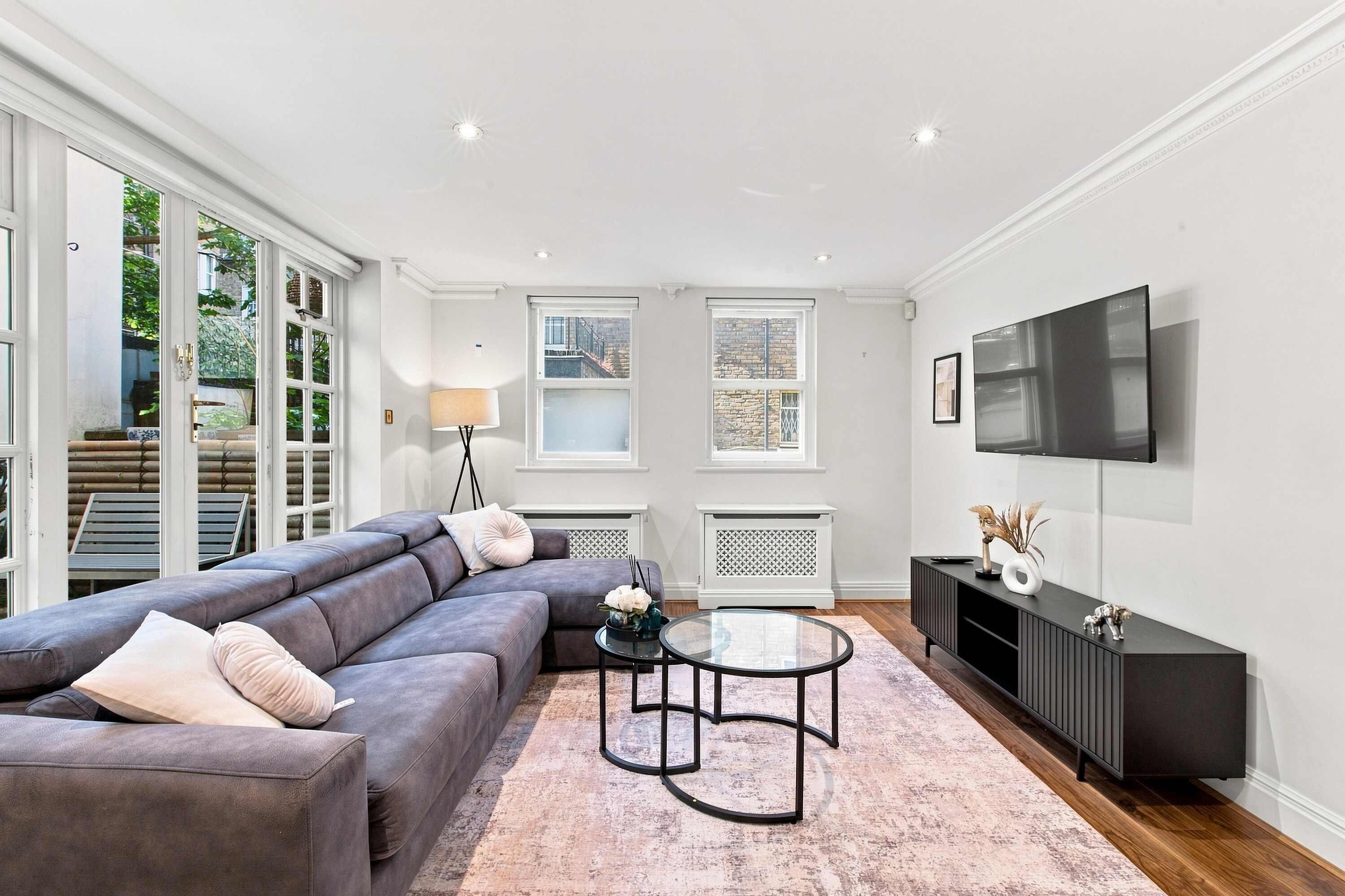 A modern living room with a sectional sofa, a glass coffee table, and a flat-screen TV mounted on the wall.