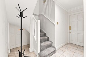 Eine Treppe mit einem Garderobenschrank am Fuß, eine Tür mit Griff und einem Lichtschalter an der Wand.