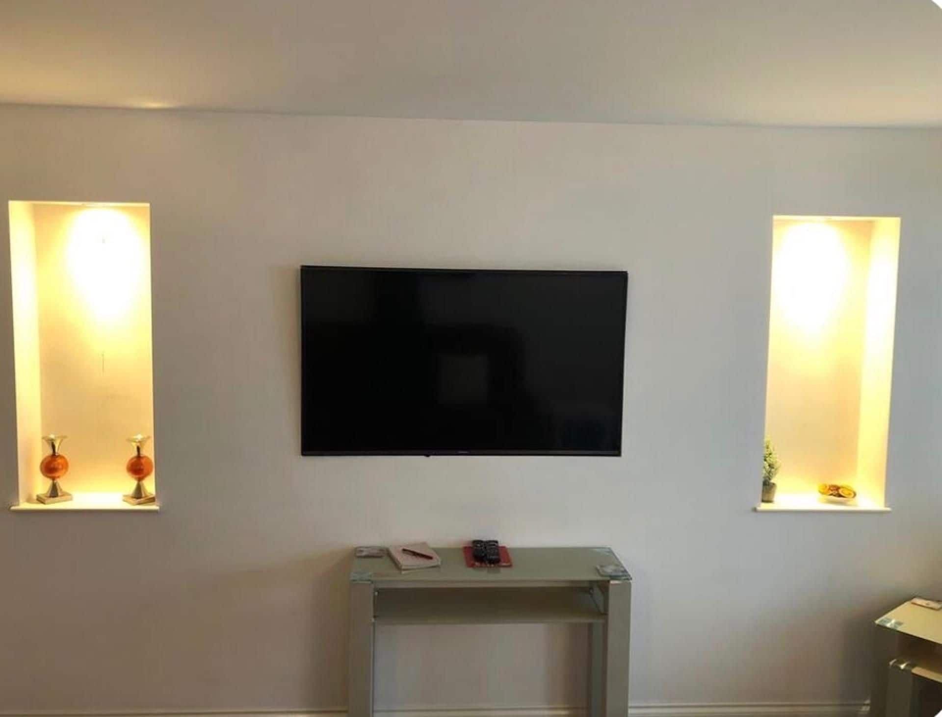 Habitación con una televisión de pantalla plana montada en la pared, flanqueada por dos lámparas de pared con estantes.