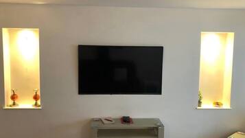Habitación con una televisión de pantalla plana montada en la pared, flanqueada por dos lámparas de pared con estantes.