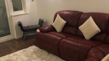 Una sala de estar con un sofá de cuero marrón oscuro, un alfombra mullida blanca y un banco.