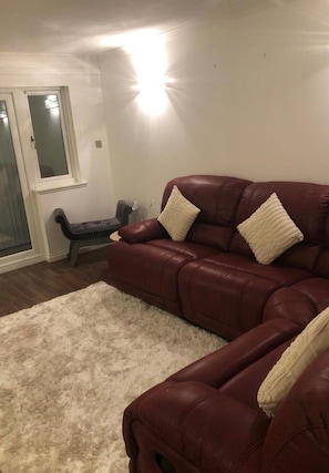 A living room with a dark brown leather sofa, a white shag rug, and a bench. - Apartment Sleeps 3 With Wifi (Alexandria)