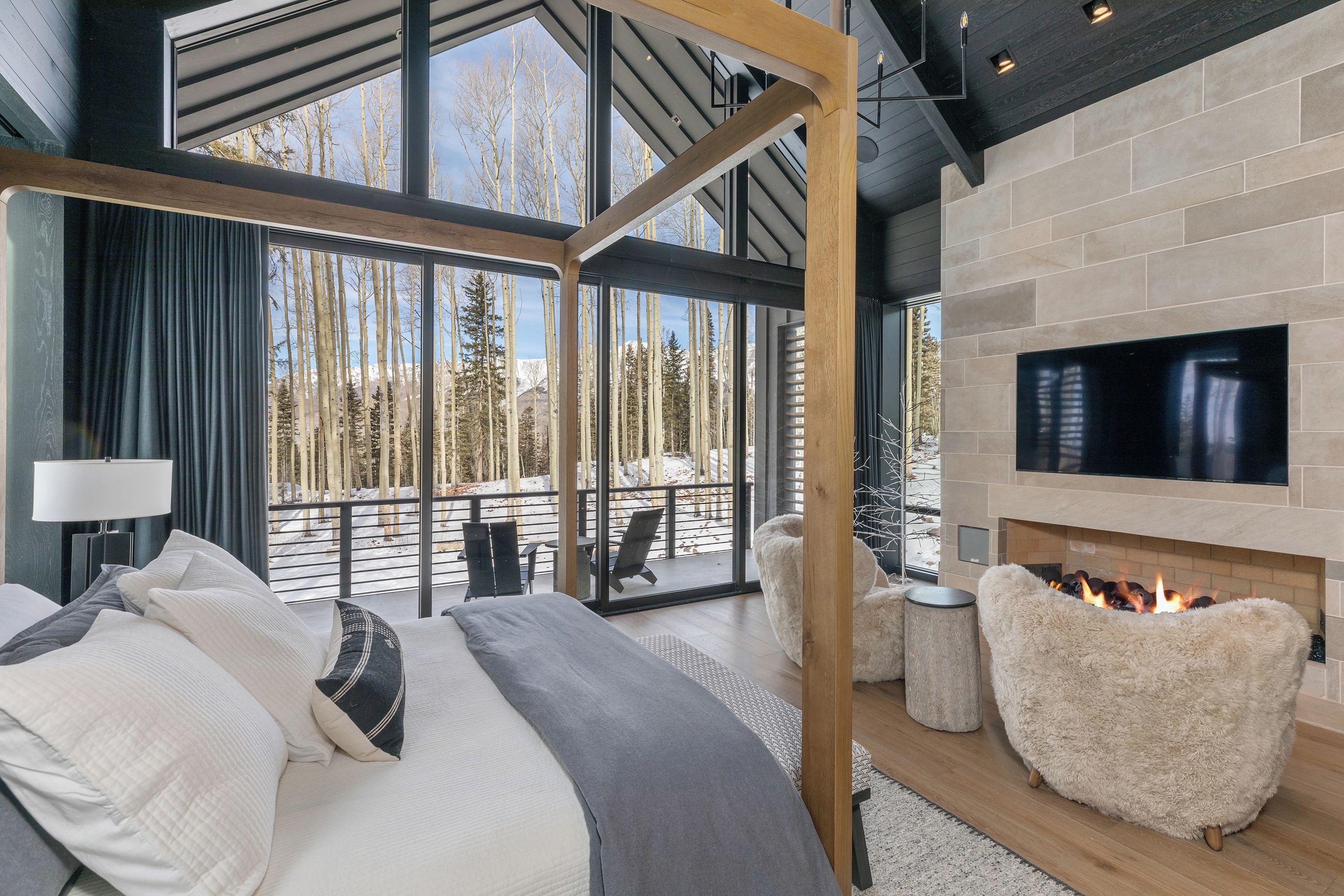 A modern bedroom with a large bed, a TV, and a fireplace.