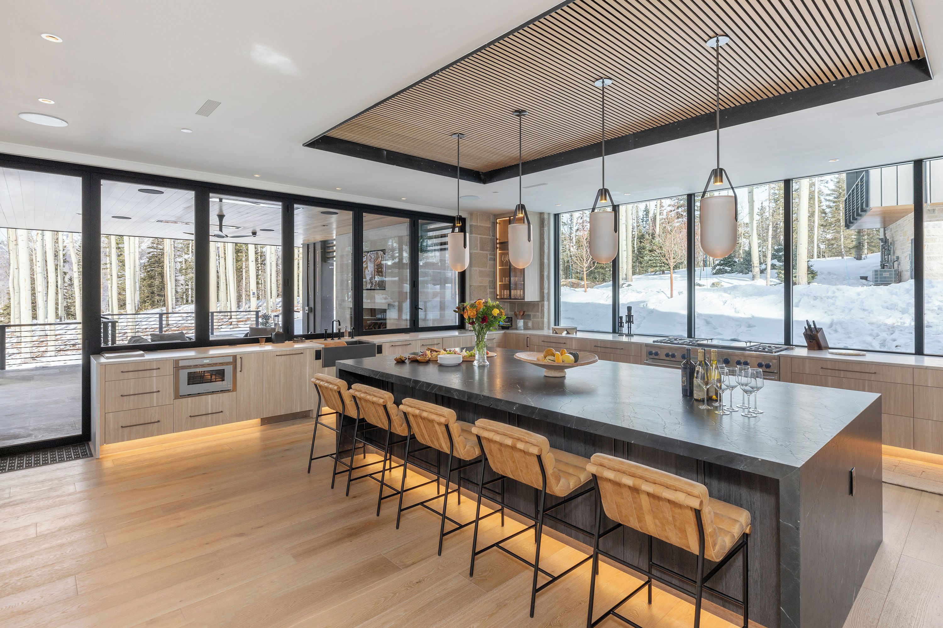 A modern kitchen with a large island, bar stools, and a view of a snowy landscape.
