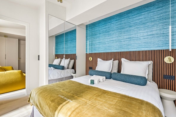 A modern hotel room with a large bed, a bedside table, a mirror, and a view of the hallway.