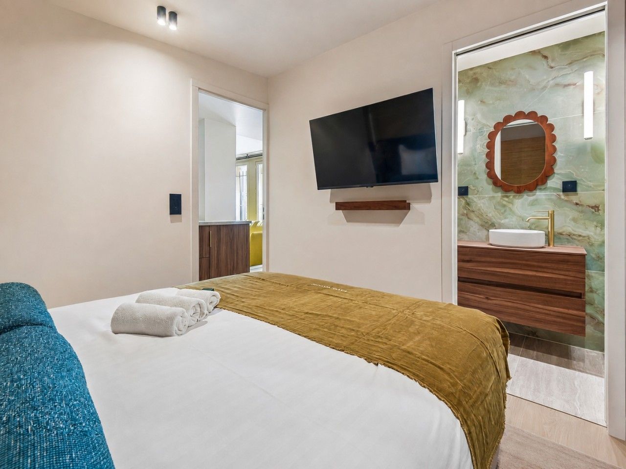 Habitación de hotel con cama, televisión, baño con espejo y lavamanos.