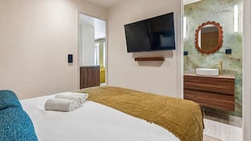 Habitación de hotel con cama, televisión, baño con espejo y lavamanos.