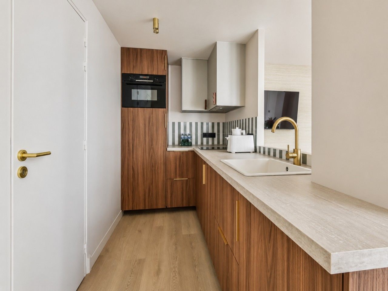 Une cuisine moderne avec des meubles en bois, un four encastré et un évier en acier inoxydable.