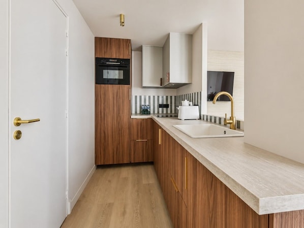 A modern kitchen with wooden cabinets, a built-in oven, and a stainless steel sink.