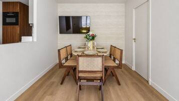 Un coin repas avec une table ronde dressée pour quatre personnes, entourée de chaises en bois dont les assises sont en osier tressé.