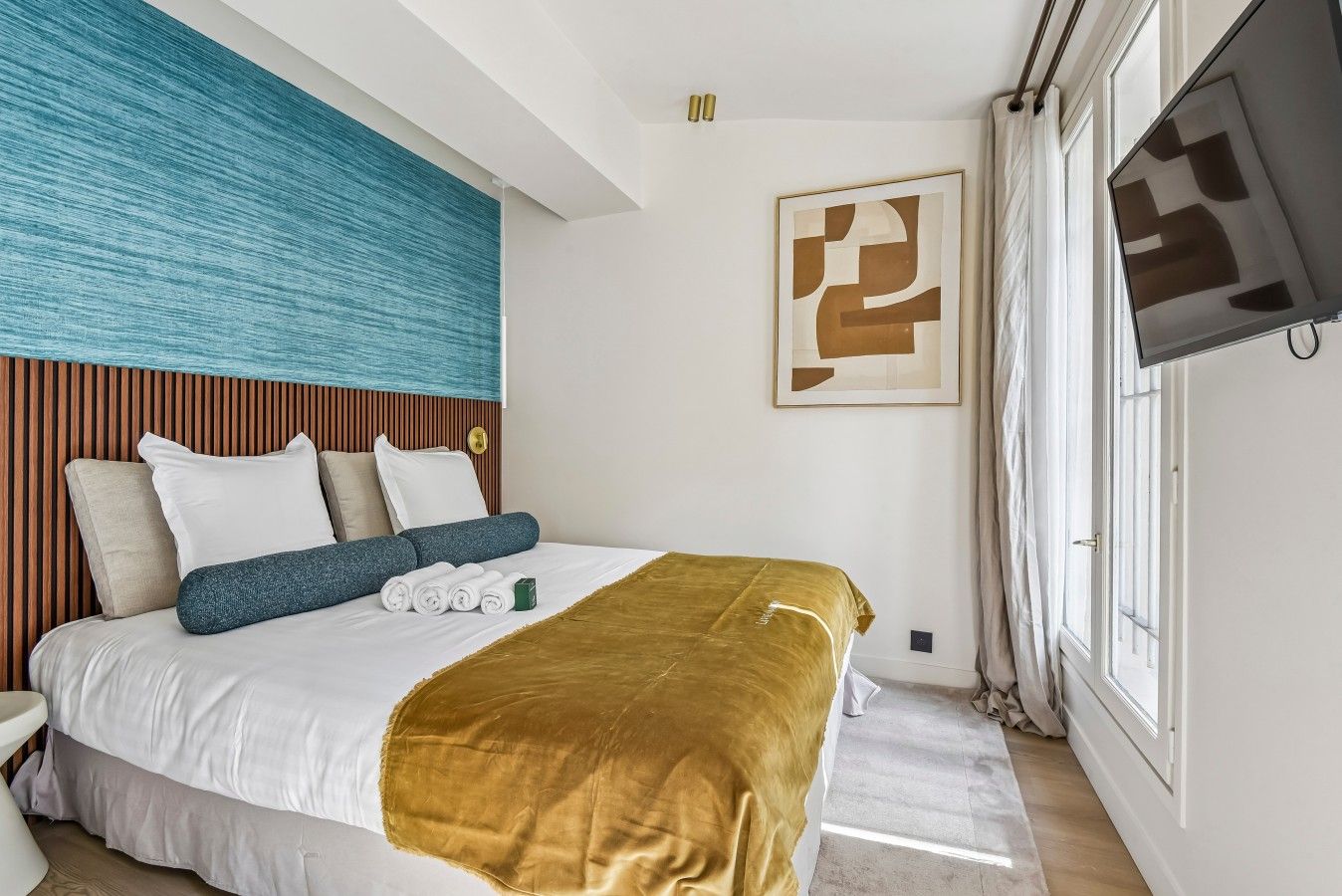 A hotel room with a bed, a television, a window, and a wall with a textured design.