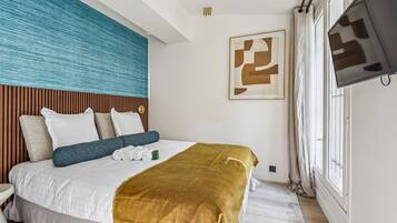 A hotel room with a bed, a television, a window, and a wall with a textured design.